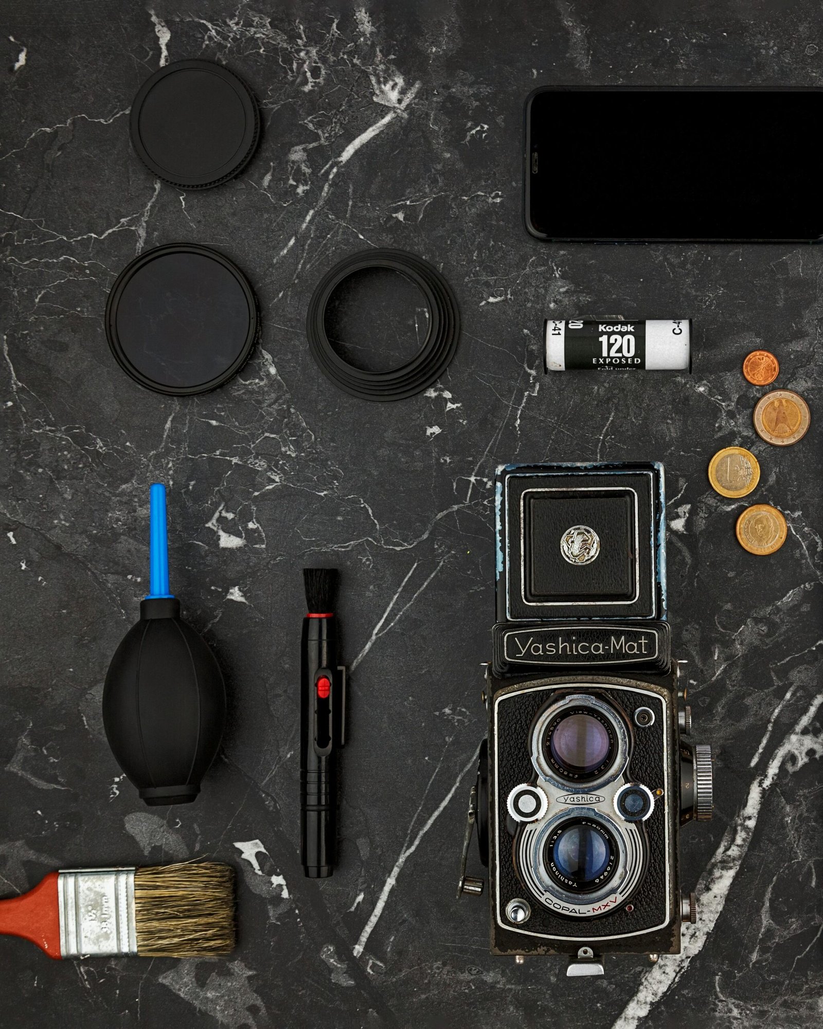 Flat lay of vintage camera, coins, and photography tools on marble surface